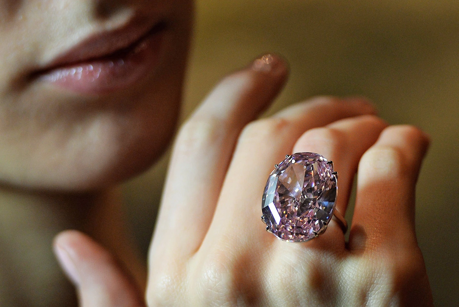 "A person wearing the Pink Star Diamond ring, showcasing the vivid pink hue and brilliance of the oval-cut gemstone on their finger